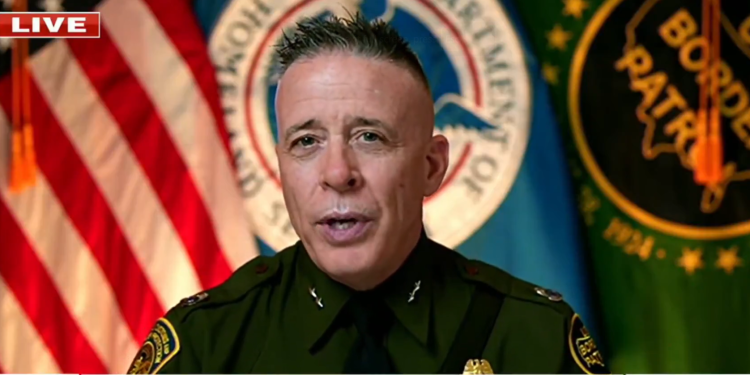 Border Commander Greg Bovino discusses CDL license fraud involving illegal immigrants beside a semi-truck on highway.