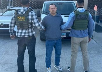 Handcuffed man being escorted by Border Patrol agents in a city.