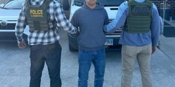 Handcuffed man being escorted by Border Patrol agents in a city.