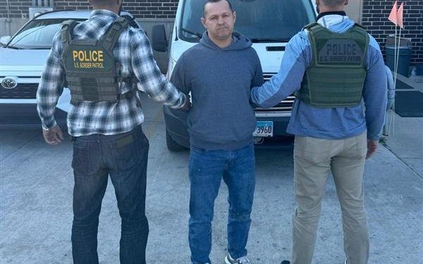 Handcuffed man being escorted by Border Patrol agents in a city.